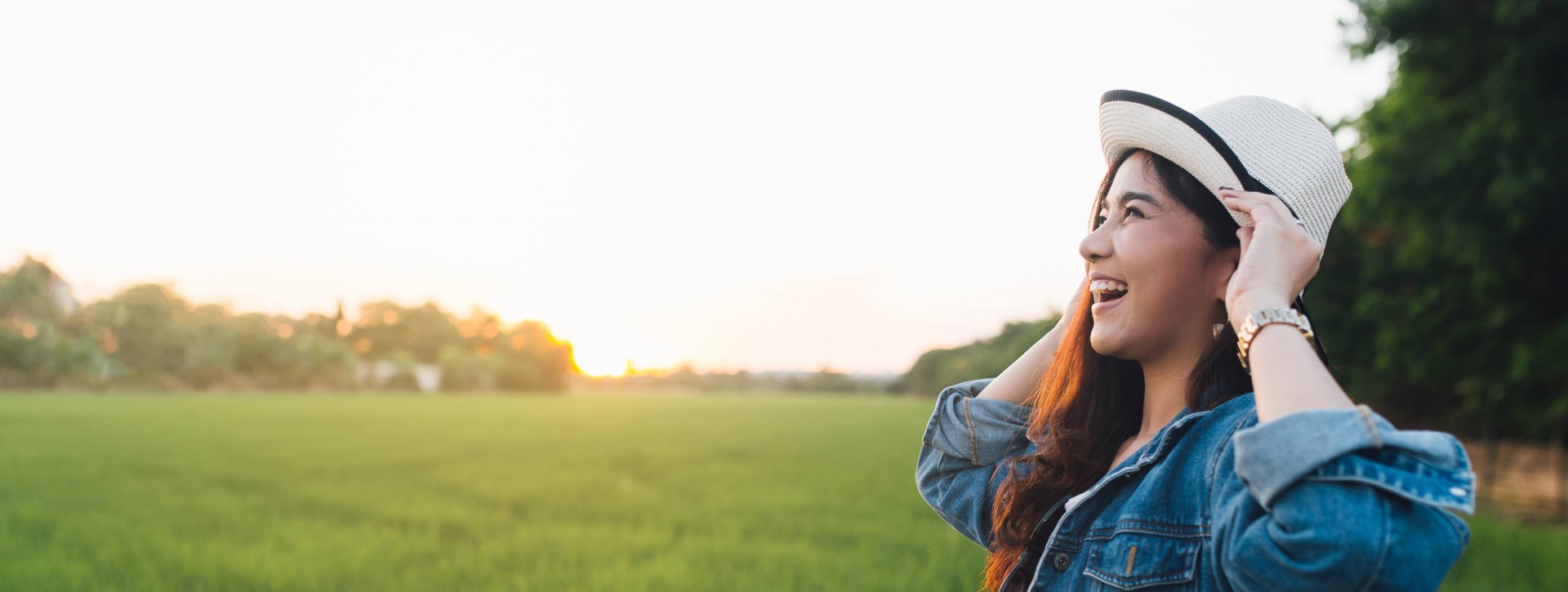 Young asian woman smiling in hat. Girl enjoying at beautiful nature with sunset.